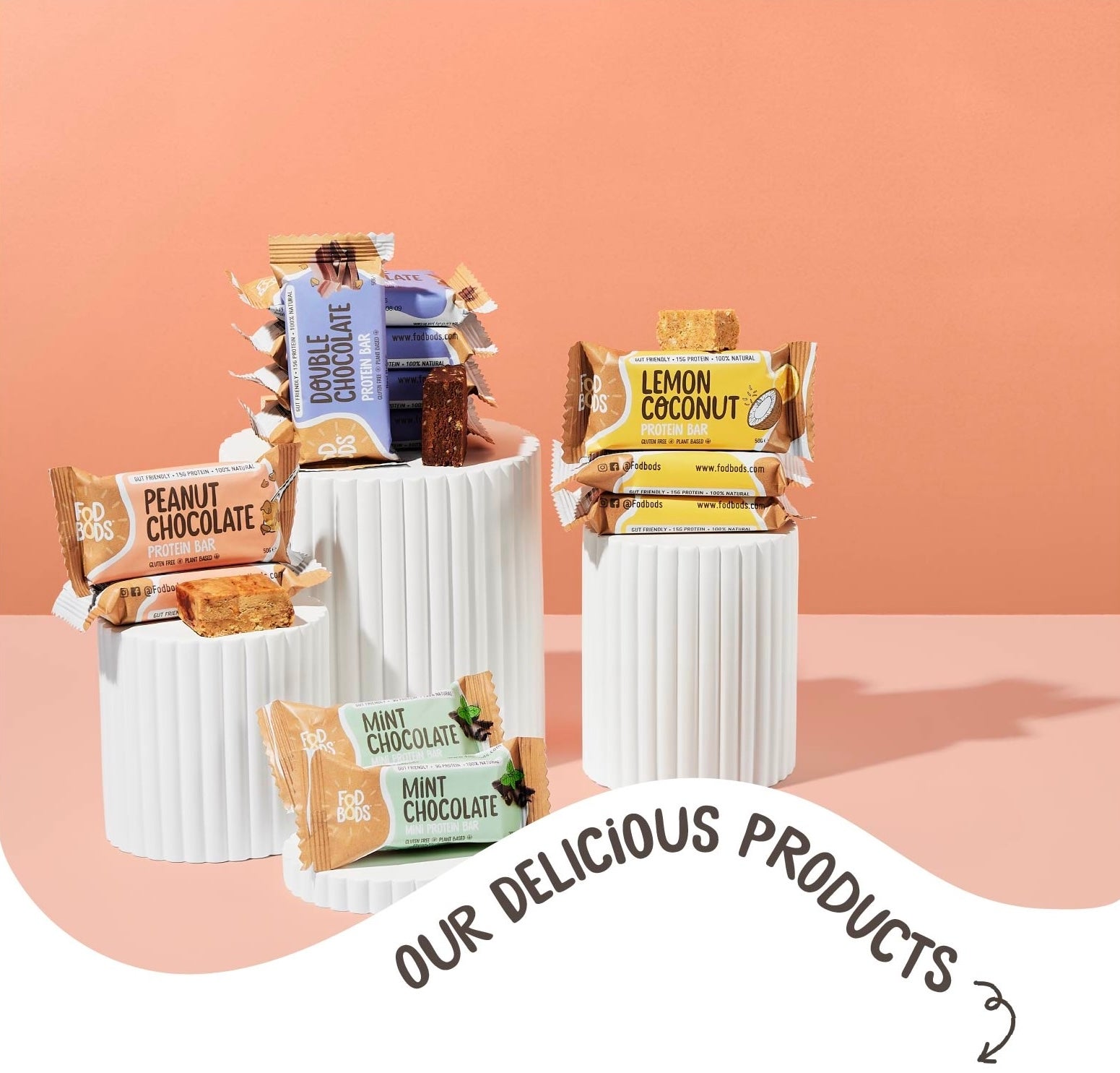 Assorted Fodbods protein bars on white cylindrical stands with a peach background 